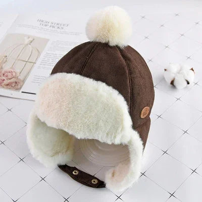 Brown winter trapper hat with white faux fur lining and pom-pom on tiled surface