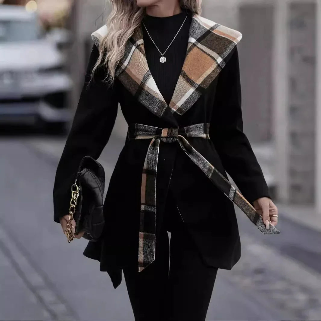 Woman wearing black coat with large tan plaid collar and belt, holding black purse with gold chain