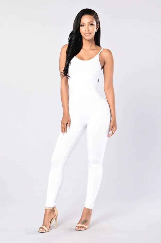 Woman in white sleeveless jumpsuit and nude heels posing on plain light background