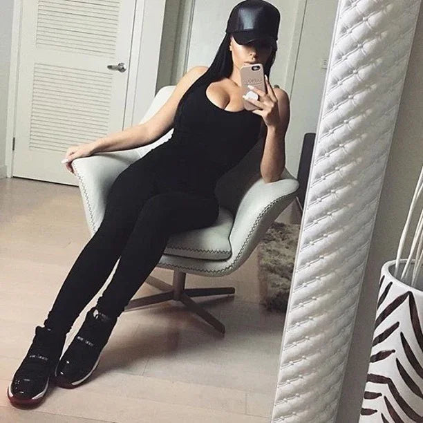 Woman in black outfit and cap taking mirror selfie in modern chair, fashion style