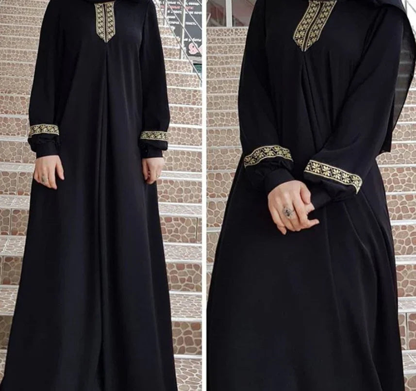Black abaya dress with gold embroidered cuffs and neckline, worn by a woman on patterned steps