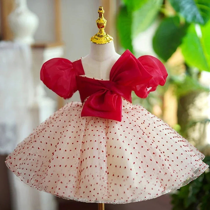 Elegant toddler dress with red puff sleeves, large bow, and white skirt with red polka dots on mannequin