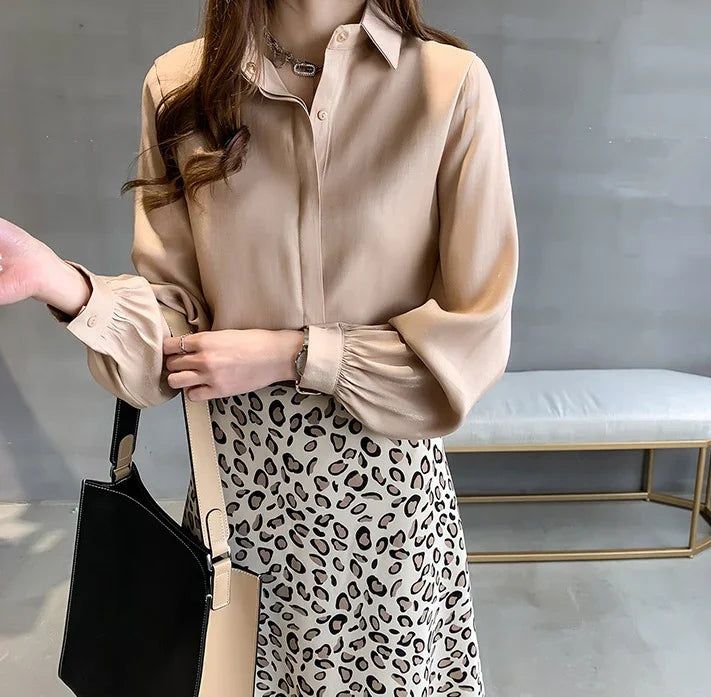 Woman wearing beige long-sleeve blouse with puff cuffs and leopard print skirt, holding black and beige handbag