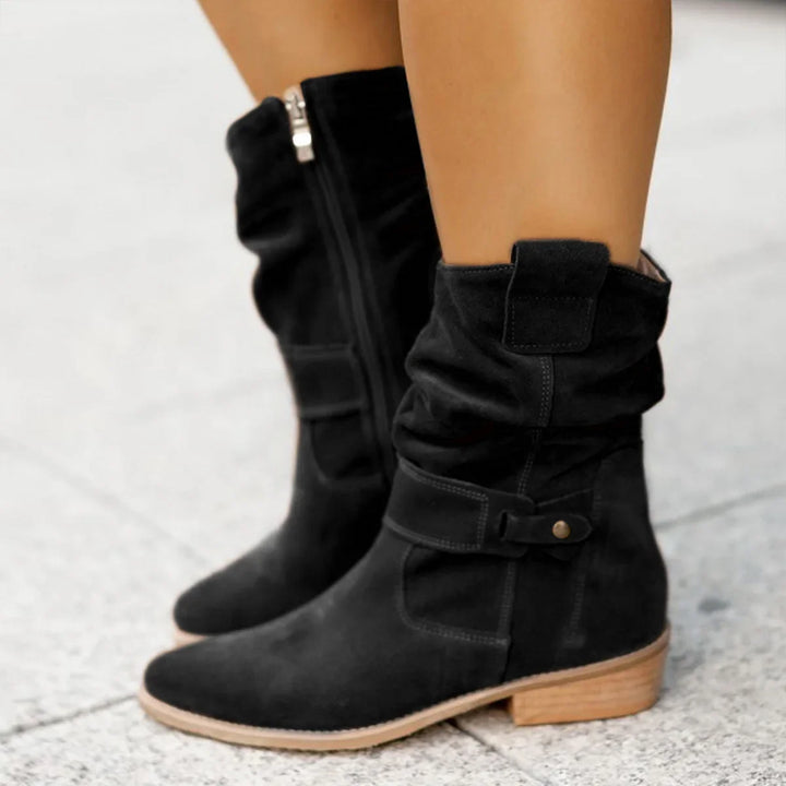 Black suede ankle boots with side zipper and wooden low heel on pavement