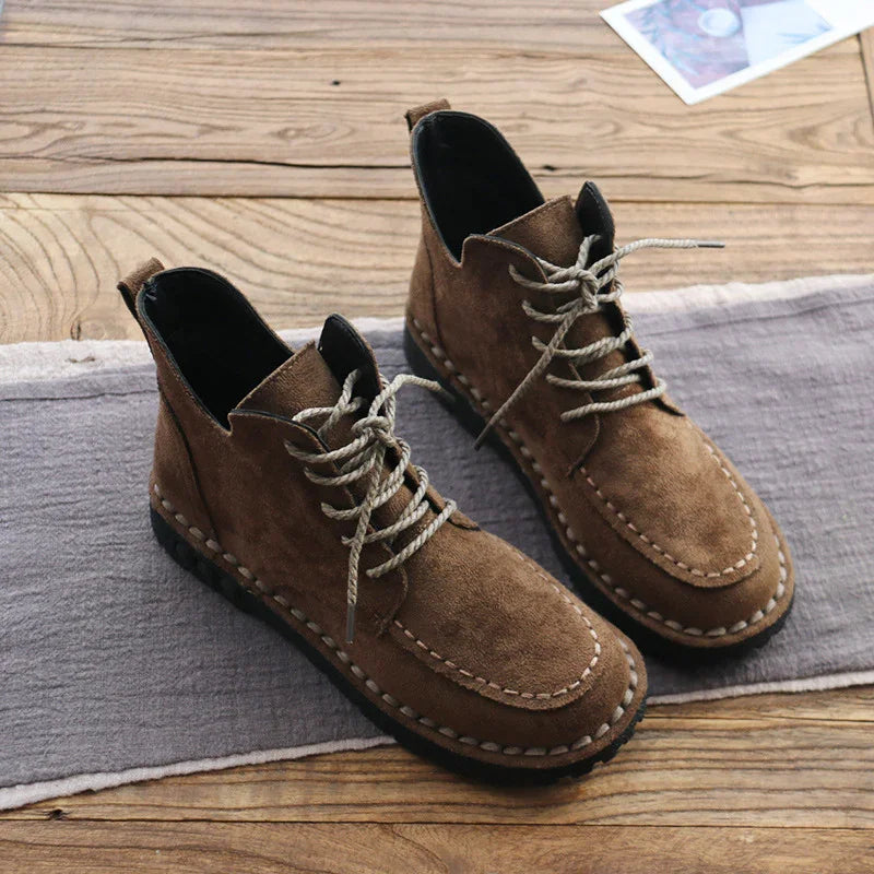 Brown suede lace-up casual boots with stitched detailing on wooden floor and gray cloth