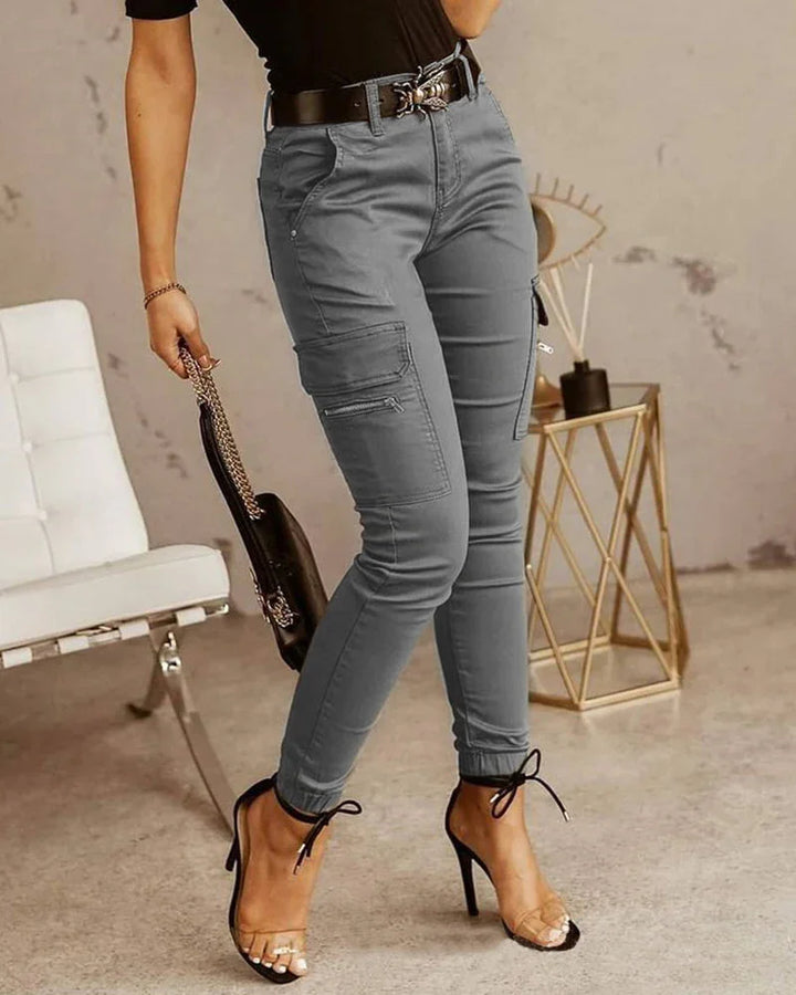 Woman wearing gray cargo pants with zipper pockets, black top, and high heel sandals indoors