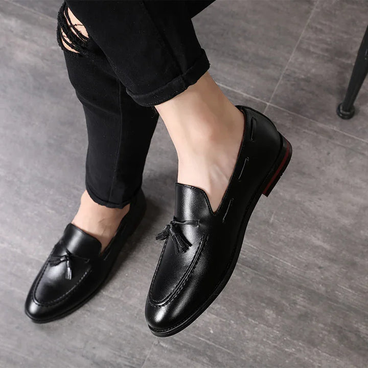 Black leather tassel loafers worn with black ripped skinny jeans on grey tile floor