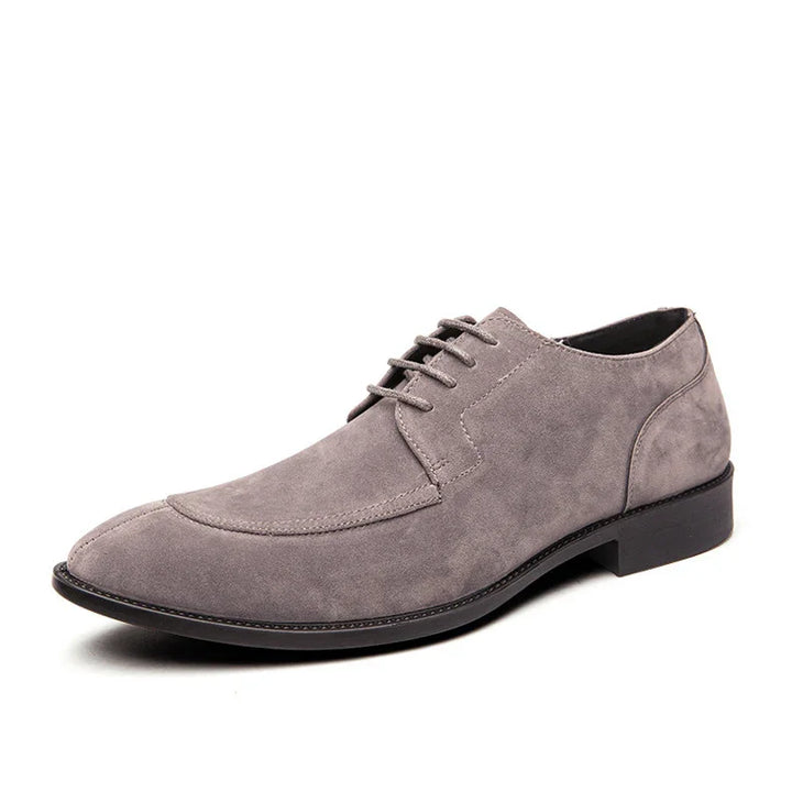 Gray suede men's dress shoe with lace-up front and black sole on white background