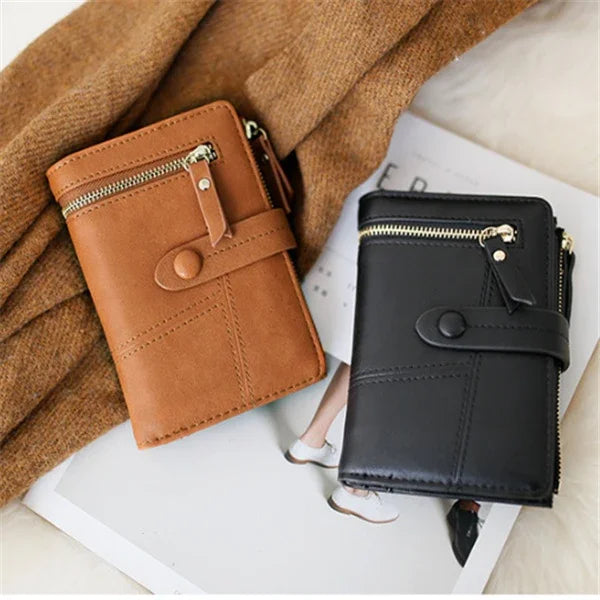 Brown and black leather wallets with zippered pockets and snap closures on soft fabric background