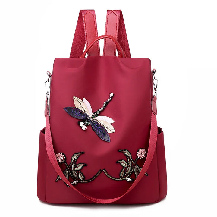 Red backpack with embroidered dragonfly and floral design, detachable shoulder strap, side pockets