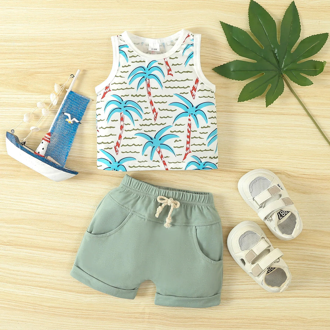 Baby summer outfit with palm tree print sleeveless top, green shorts, and white sandals on wood