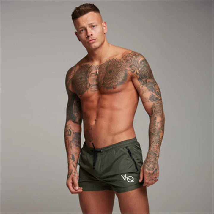 Muscular tattooed man wearing green VQ brand shorts on gray background