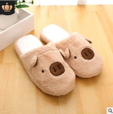 Cozy beige plush slippers with pig face design on wooden floor near white box and green plant