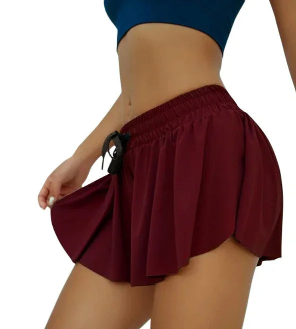 Woman wearing maroon athletic skirt with black drawstring and blue sports bra, side view on white background