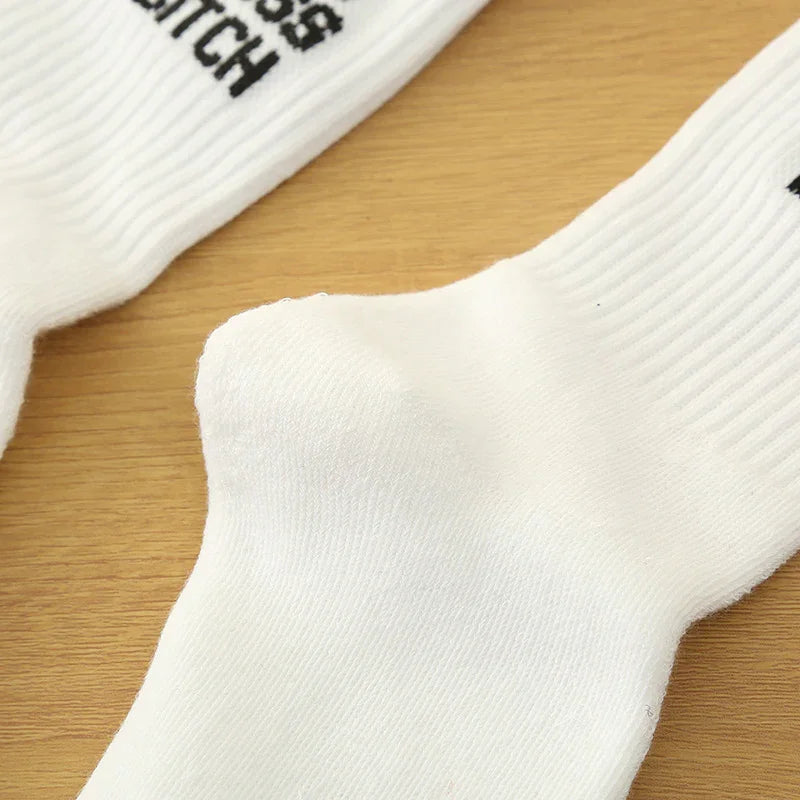 Close-up of white crew socks on wooden surface with black text branding