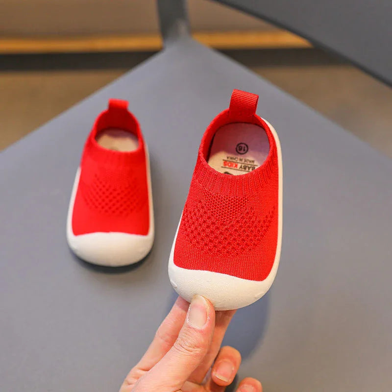Pair of red baby shoes with white soles on gray surface, one held by hand