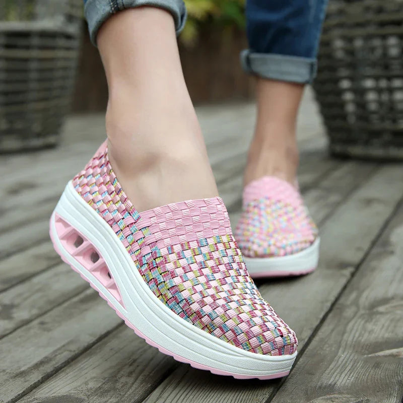 Close-up of feet wearing pink woven platform slip-on sneakers with air cushion sole on wooden deck