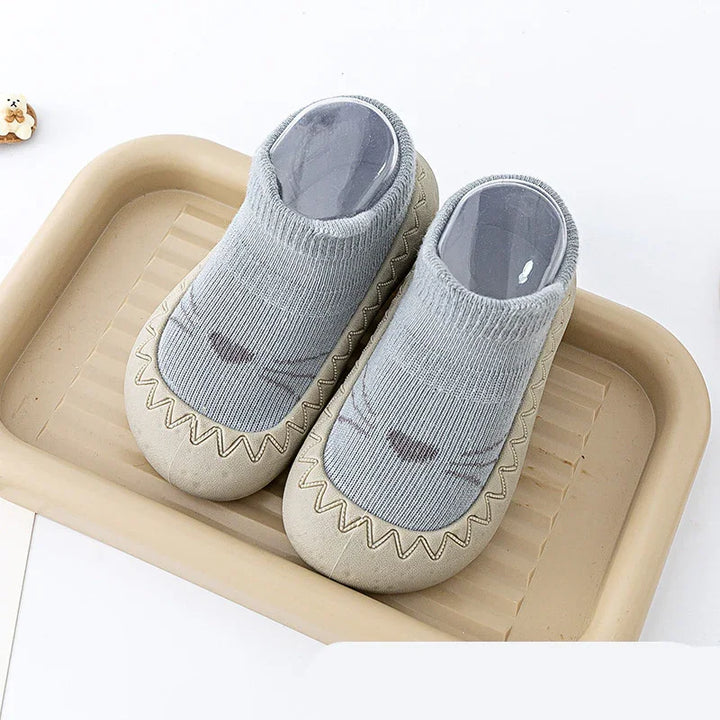 Gray baby socks with cat face design and beige rubber soles on a beige tray