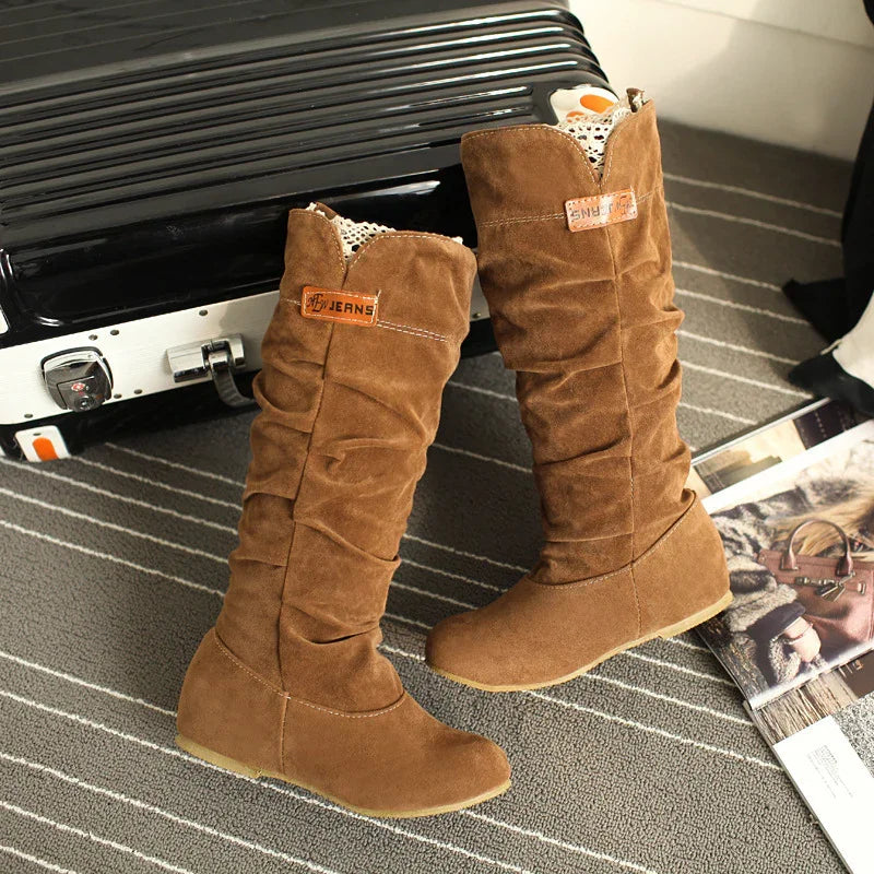 Brown suede slouchy knee-high boots with lace trim, on gray striped carpet near black suitcase