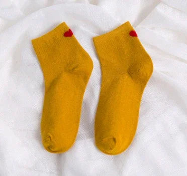 Pair of yellow ankle socks with small red heart detail on white fabric background