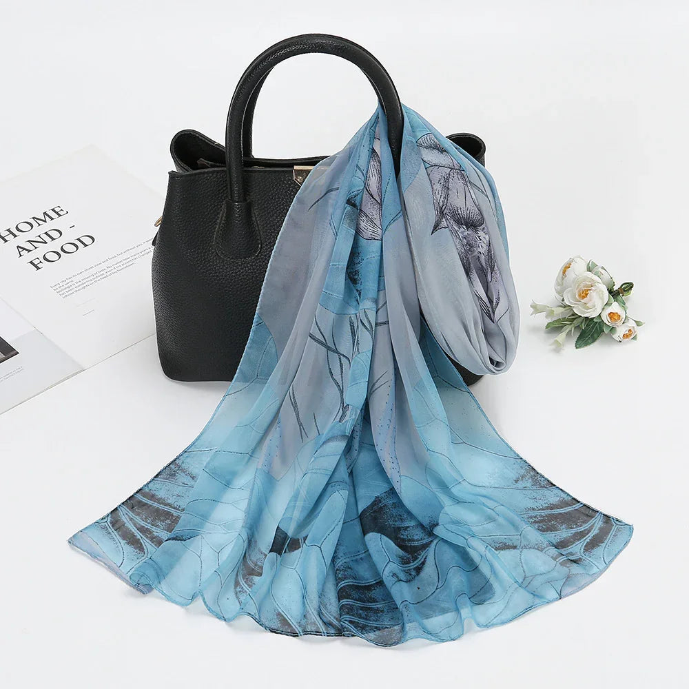 Black leather handbag with blue floral silk scarf draped over handle on white surface