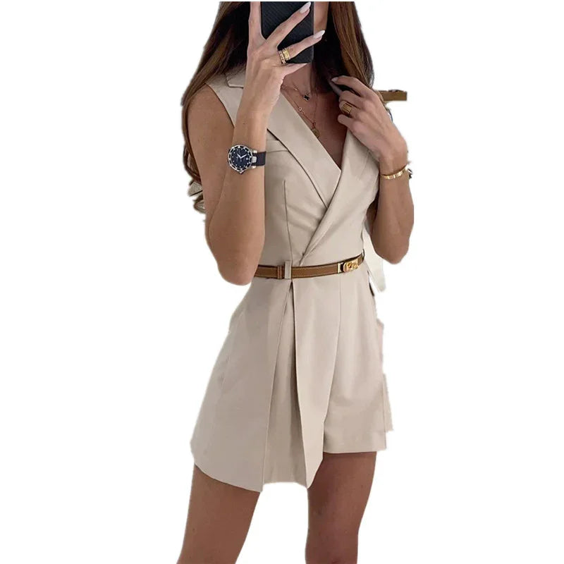 woman wearing beige sleeveless belted blazer dress with watch and gold jewelry taking a mirror selfie