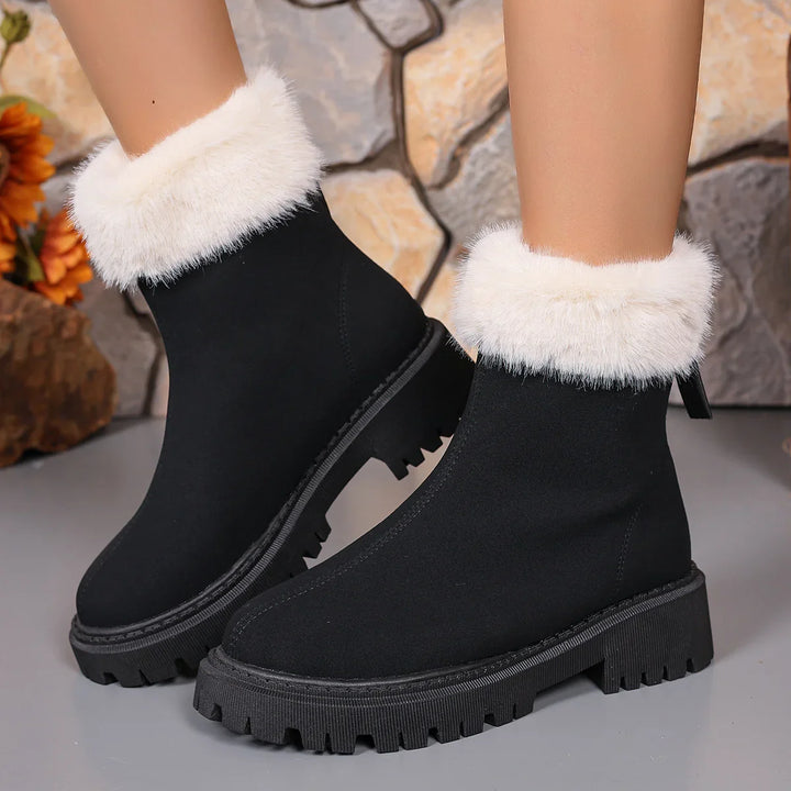 Black winter boots with thick soles and white faux fur cuffs on model feet against stone background