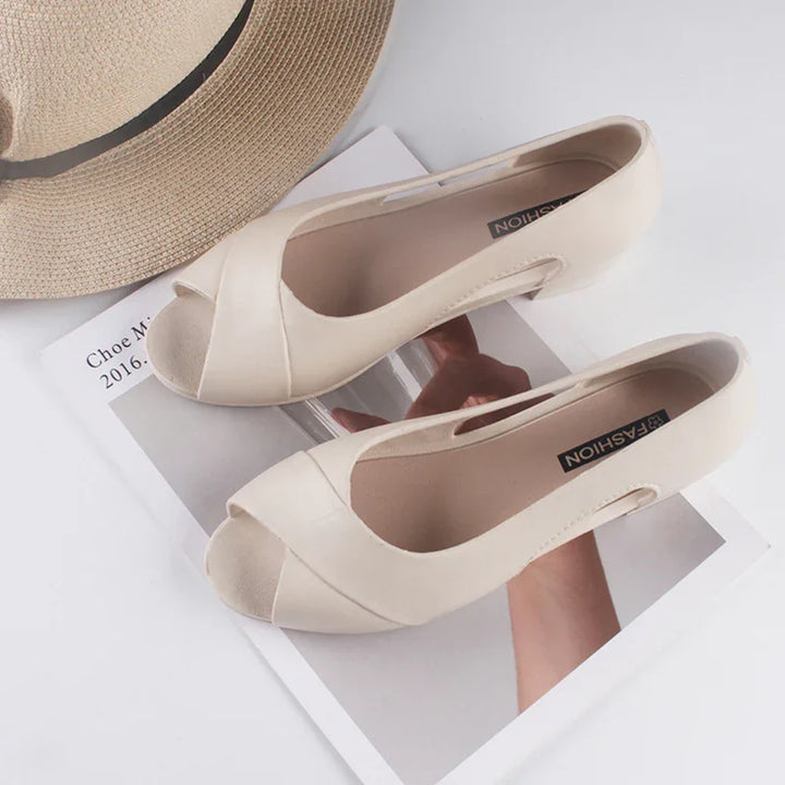 Beige peep-toe flats on a magazine page next to a woven straw hat with black trim