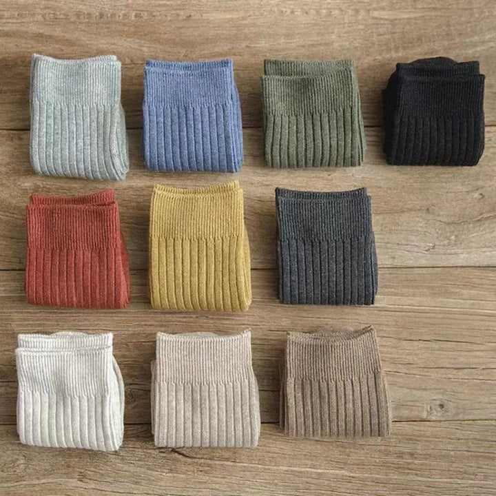 Nine pairs of colorful ribbed knit socks neatly folded on wooden surface