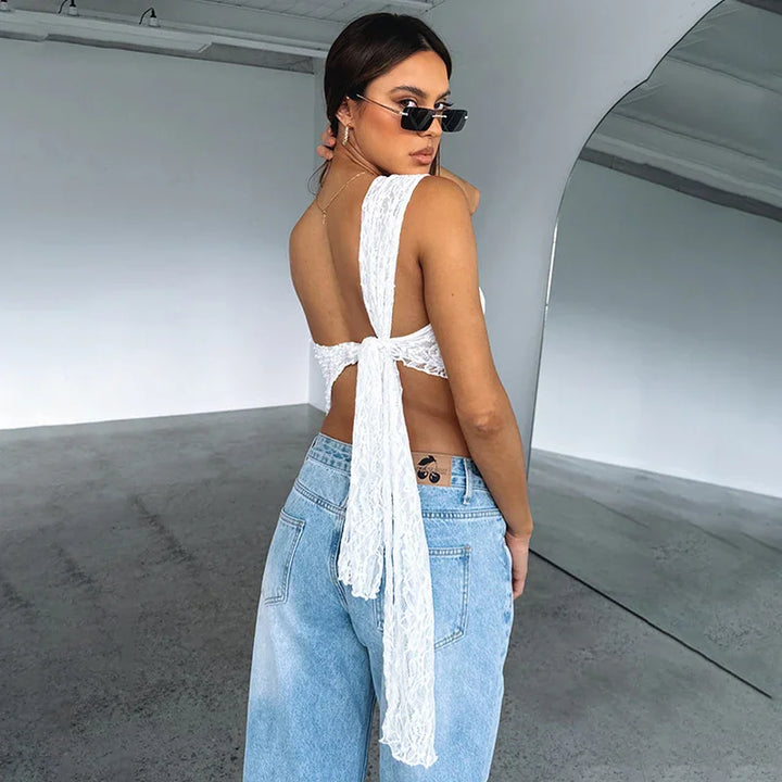 Woman wearing white lace backless top and light blue jeans with sunglasses in a modern minimal indoor space