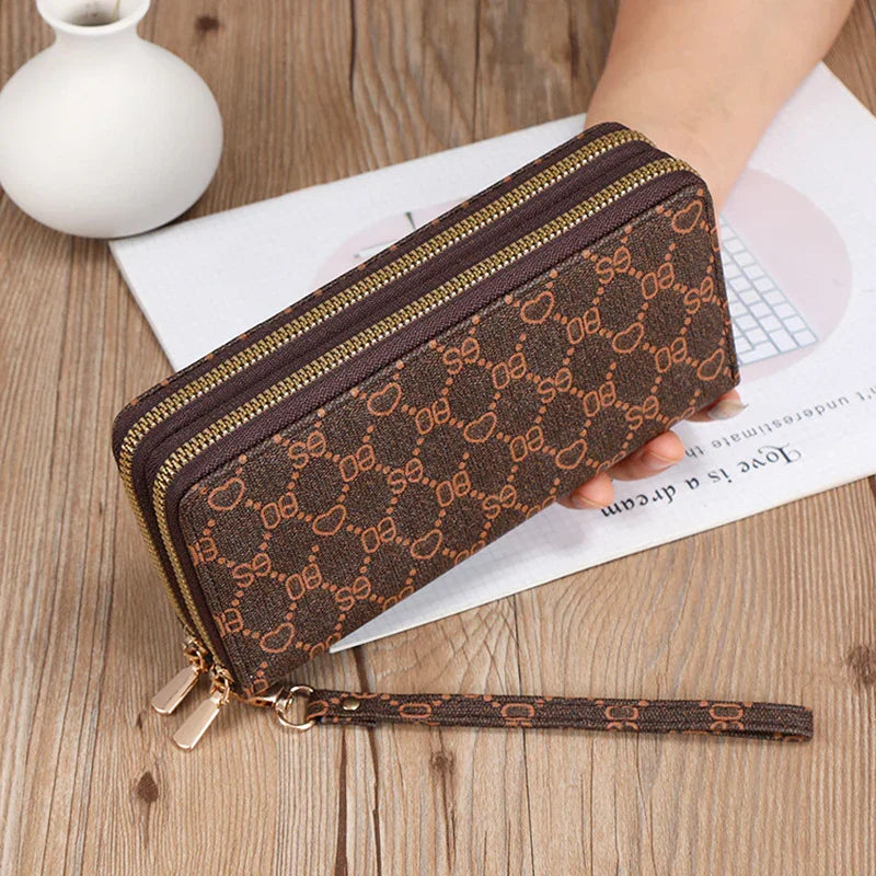 Brown patterned zippered wristlet wallet with gold-tone hardware on wooden surface