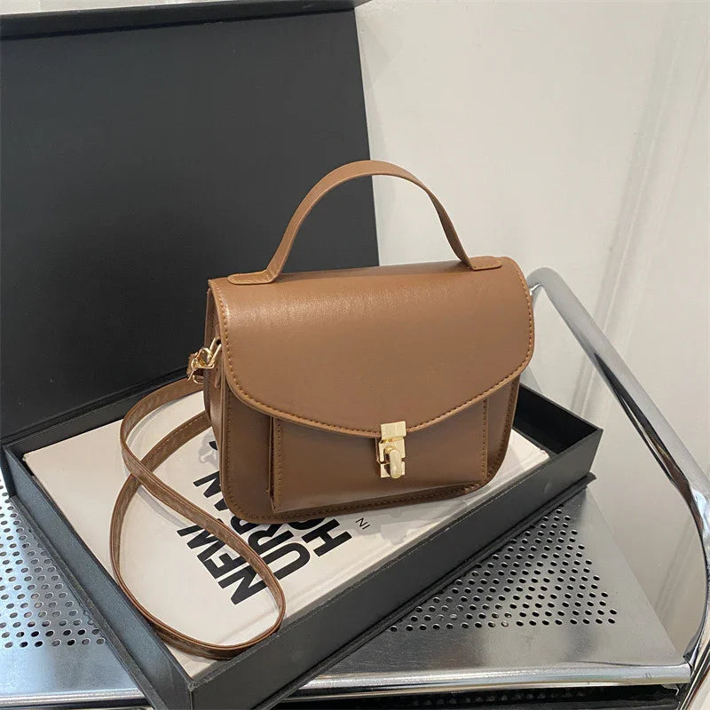 Brown leather crossbody handbag with top handle and gold clasp on black tray