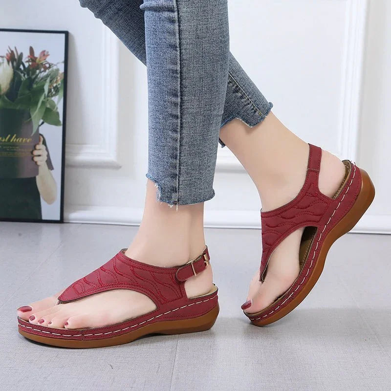 Woman wearing red leather sandals with buckle straps and brown soles, paired with cropped blue jeans
