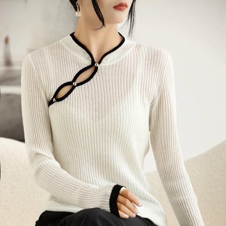 Woman wearing elegant white ribbed sweater with black trim and pearl button cutout detail