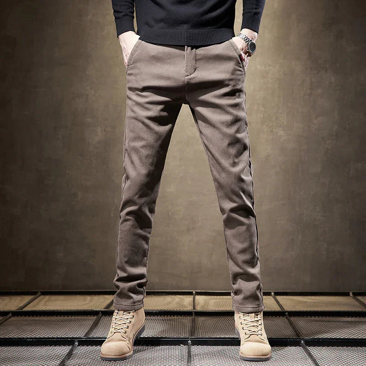 Man wearing slim fit brown casual pants and beige lace-up boots standing on metal grid floor