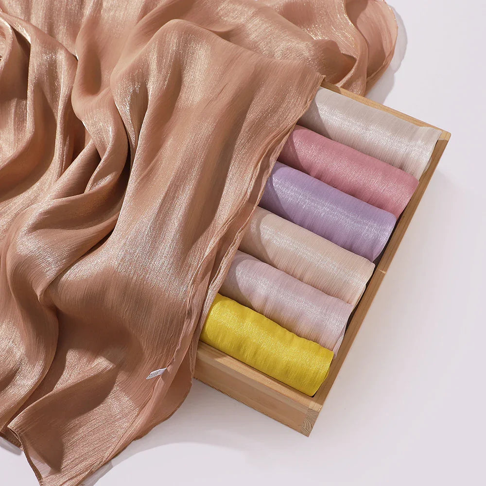 Shiny soft fabric scarves in pastel colors displayed in wooden box with one draped outside