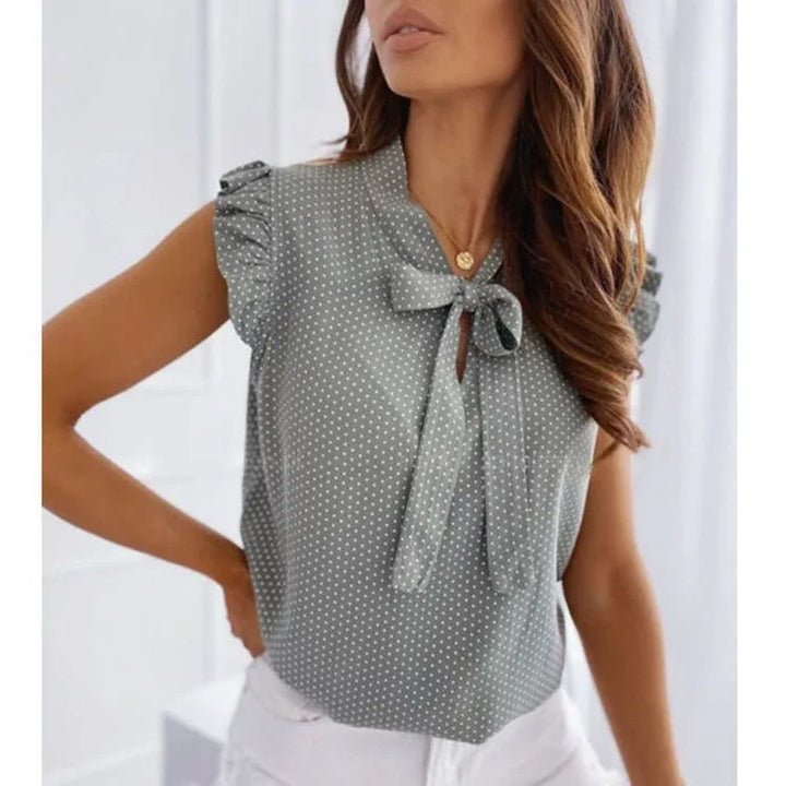 Woman wearing sleeveless gray polka dot blouse with bow tie neck and ruffled shoulders