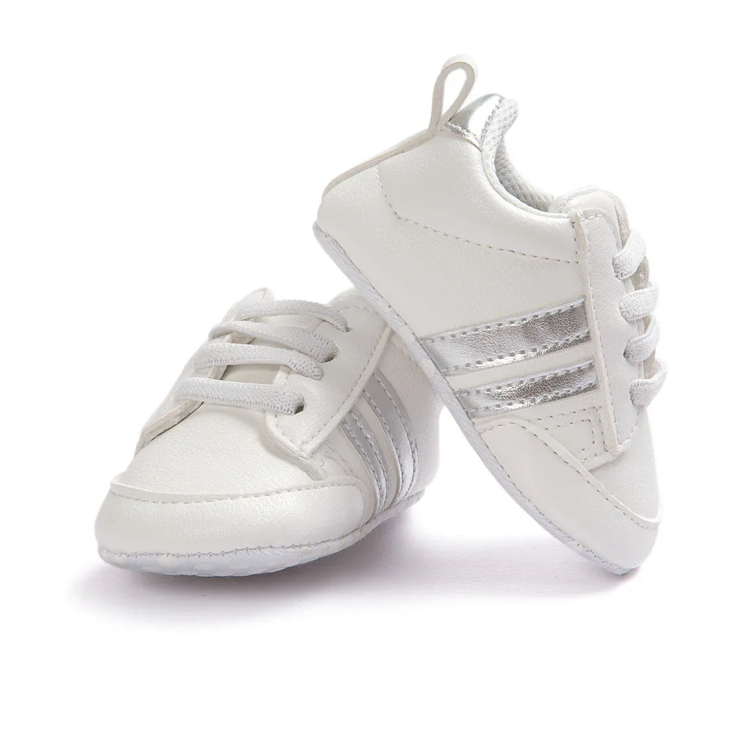 White baby sneakers with silver stripes and white laces on a white background