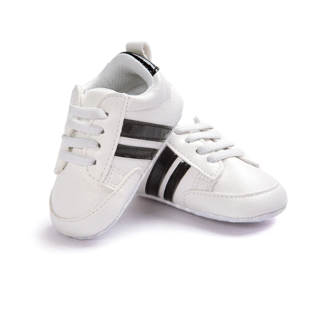 White baby sneakers with black stripes and laces on a white background
