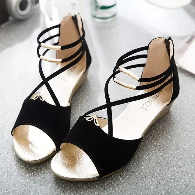 Black and gold open-toe wedge sandals with crisscross ankle straps on a gray surface