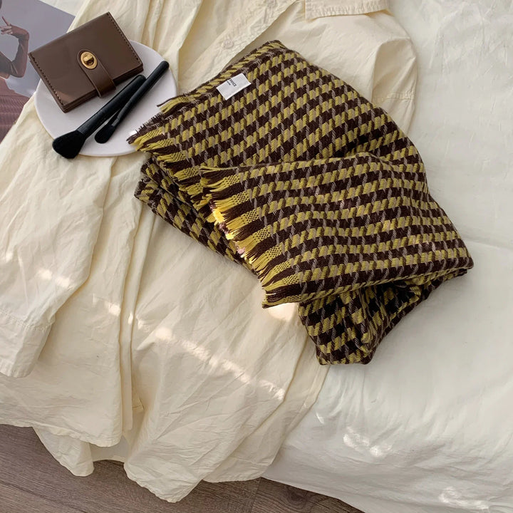 Folded brown and yellow checkered scarf on cream fabric shirt with brown wallet and black makeup brushes