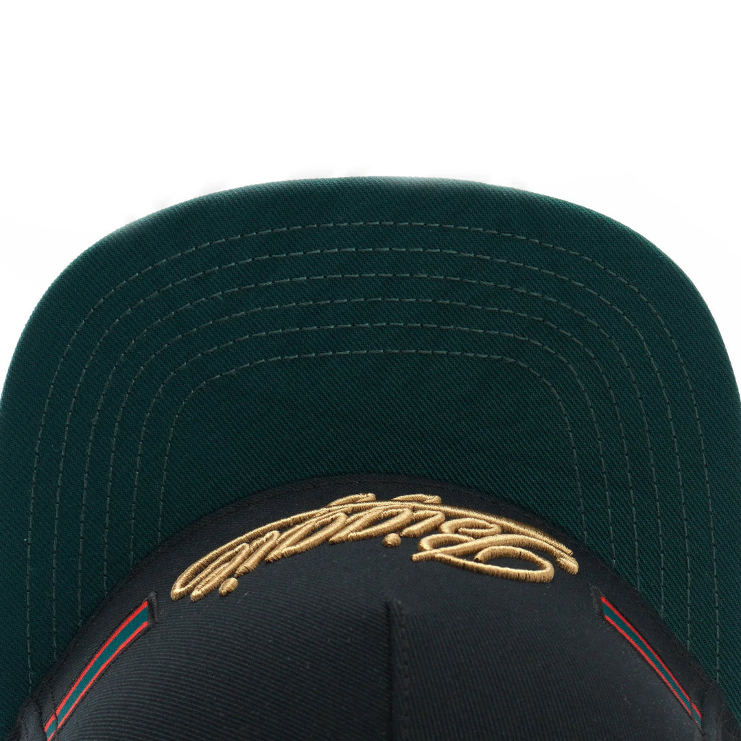 Black baseball cap with green underbill and gold embroidered signature on front