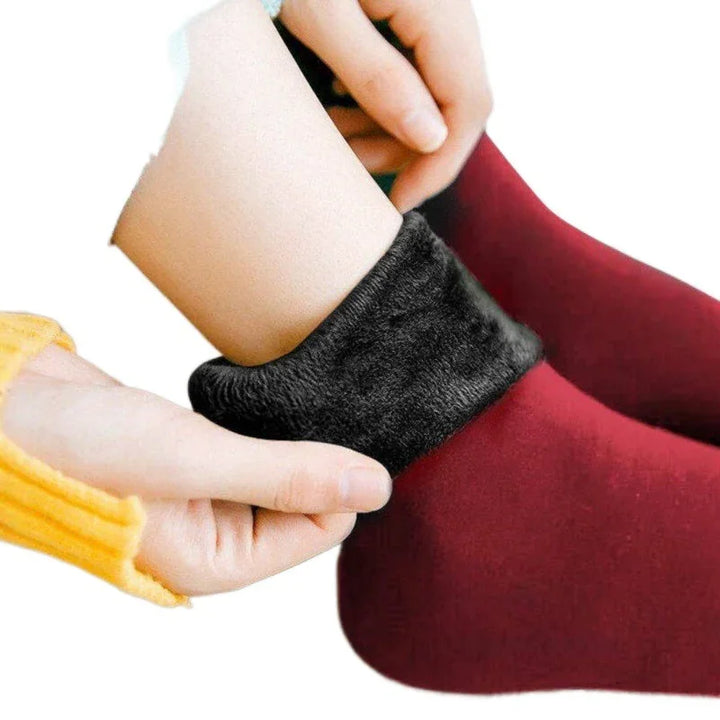 Hands adjusting warm black fuzzy lined red socks on feet against white background