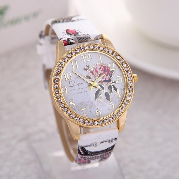 Elegant gold-tone wristwatch with crystal bezel, floral dial, and patterned white leather strap