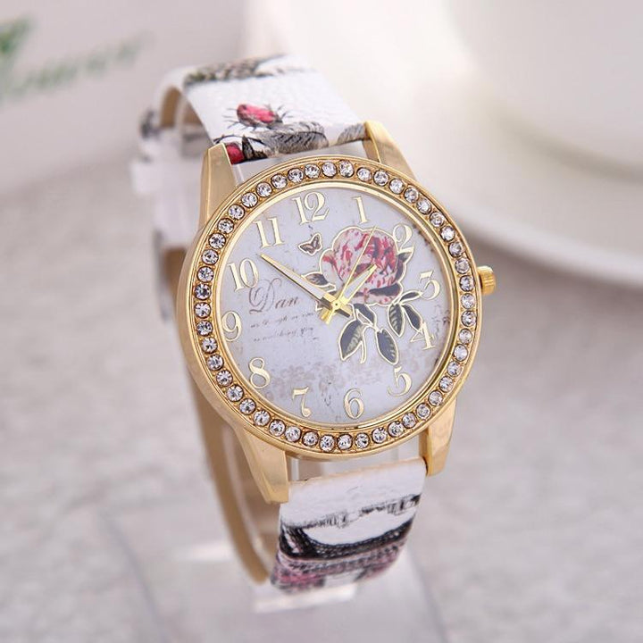 Elegant gold-tone wristwatch with crystal bezel, floral dial, and patterned white leather strap