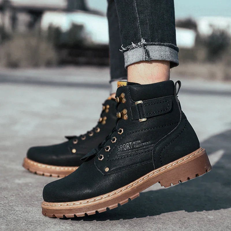 Black sport work boots with brown soles and gold eyelets worn with rolled-up dark jeans outdoors