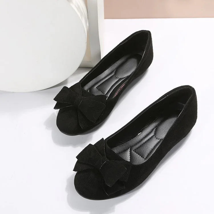 Pair of black suede women's flats with large bows on the toes on a white surface