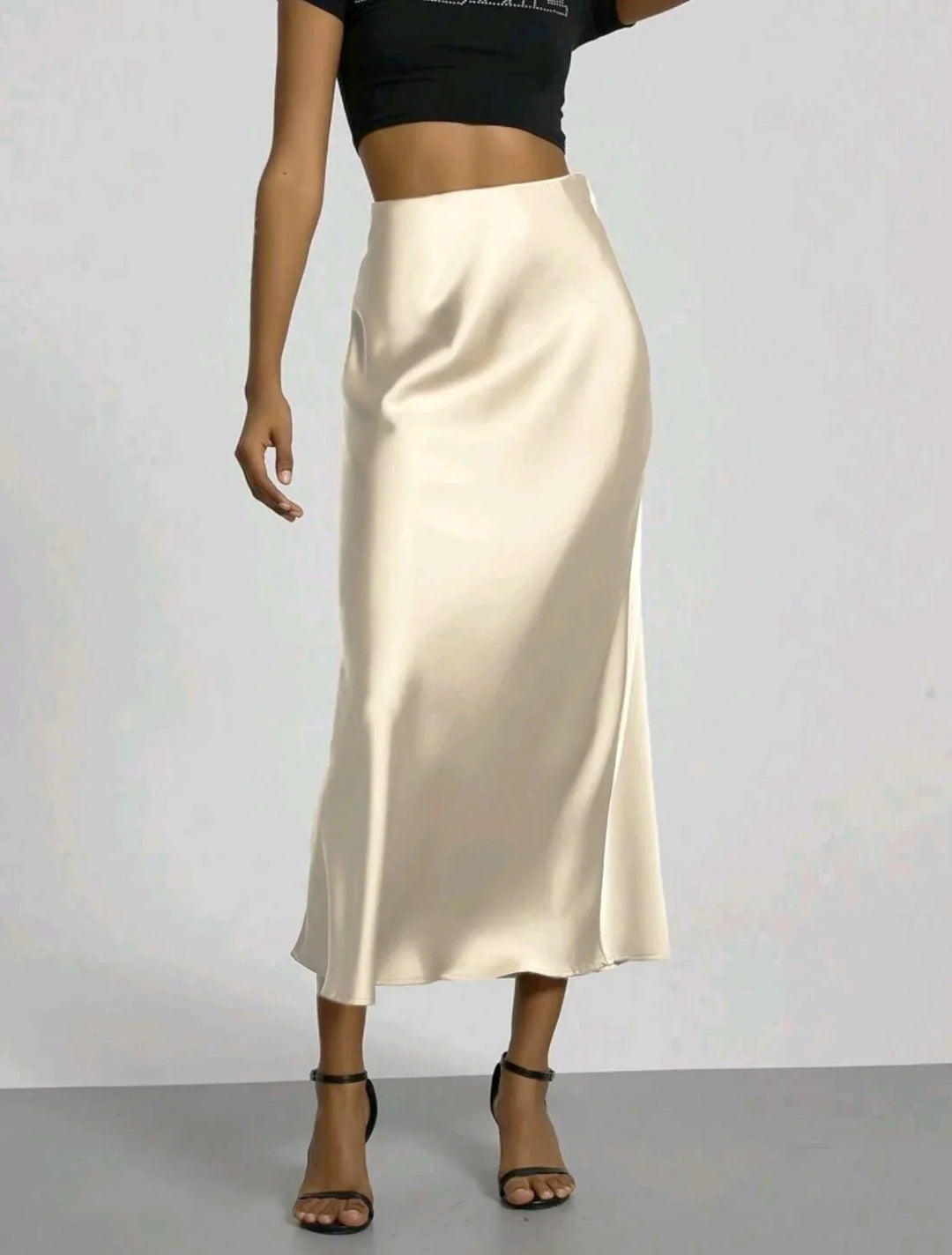 Woman wearing a cream satin midi skirt paired with black crop top and black strappy heels
