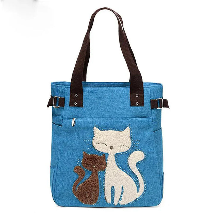 blue tote bag with brown handles featuring embroidered white and brown cats design