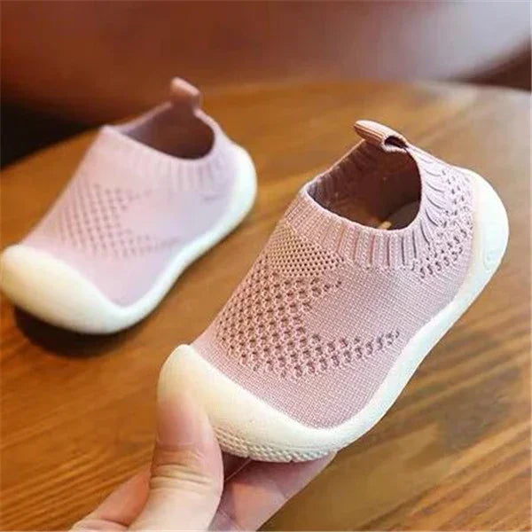 Soft pink knitted slip-on baby shoes with white rubber soles on wooden surface